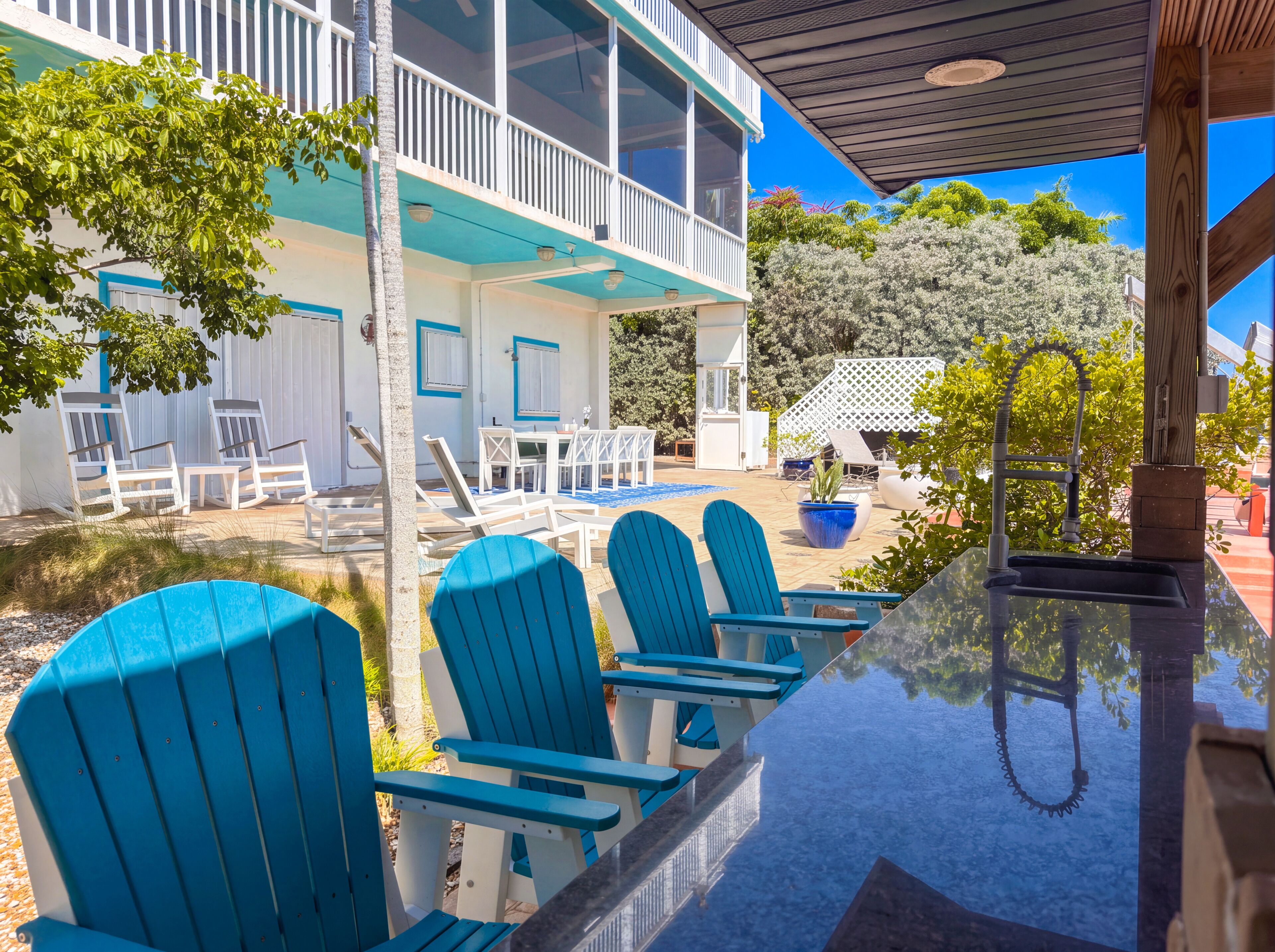 A poolside area with blue chairs and a table, a covered seating area, and a building with a balcony.