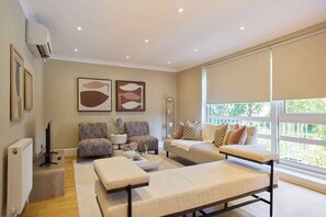 A modern living room with a sofa, armchairs, a coffee table, and a large window with a view. - Well Placed in the Wood (Greater London)