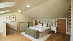 A bedroom with a bed, bedside tables, a nightstand, a wardrobe, a staircase, and a door. - Well Placed in the Wood (Greater London)