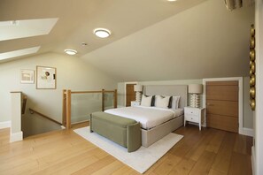 A bedroom with a bed, bedside tables, a nightstand, a wardrobe, a staircase, and a door. - Well Placed in the Wood (Greater London)