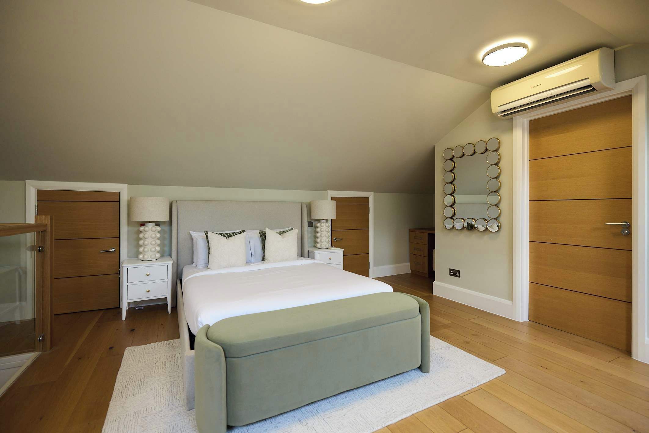 A bedroom with a bed, bedside tables, a mirror, an air conditioning unit, and a wooden wardrobe.