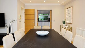 A conference room with a long table, white chairs, a white bowl, a wooden door, and a kitchen visible through an open door. - Well Placed in the Wood (Greater London)