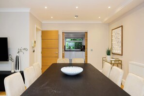 A conference room with a long table, white chairs, a white bowl, a wooden door, and a kitchen visible through an open door. - Well Placed in the Wood (Greater London)