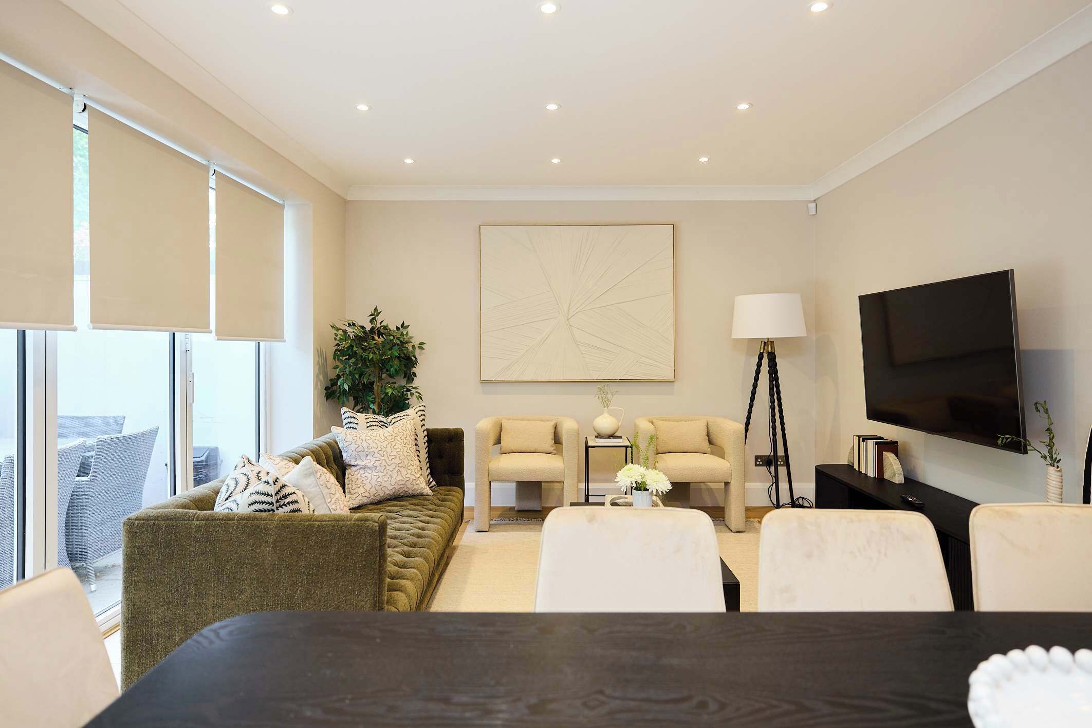 A modern living room with a sofa, armchairs, a coffee table, a TV, and a large window.