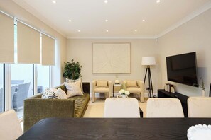 A modern living room with a sofa, armchairs, a coffee table, a TV, and a large window. - Well Placed in the Wood (Greater London)