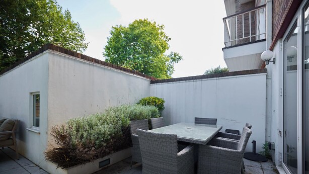 A patio with a table and chairs, a small window, and a white wall. - Well Placed in the Wood (Greater London)