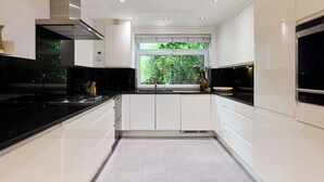 A modern kitchen with white cabinetry, black countertops, a stainless steel range hood, and a window with a view of greenery. - Well Placed in the Wood (Greater London)