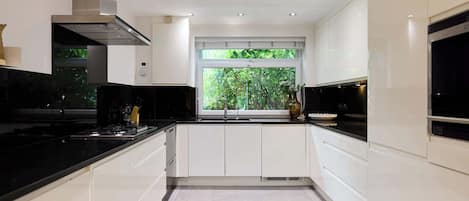 A modern kitchen with white cabinetry, black countertops, a stainless steel range hood, and a window with a view of greenery.