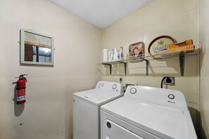 A laundry room with two white washers and dryers, a fire extinguisher, a shelf with cleaning supplies, and a framed picture on the wall. - Cozy A-Frame Steps from Downtown Banner Elk (Banner Elk)