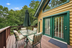 A wooden deck with a glass table and chairs, a green umbrella, and a door with a window. - Cozy A-Frame Steps from Downtown Banner Elk (Banner Elk)