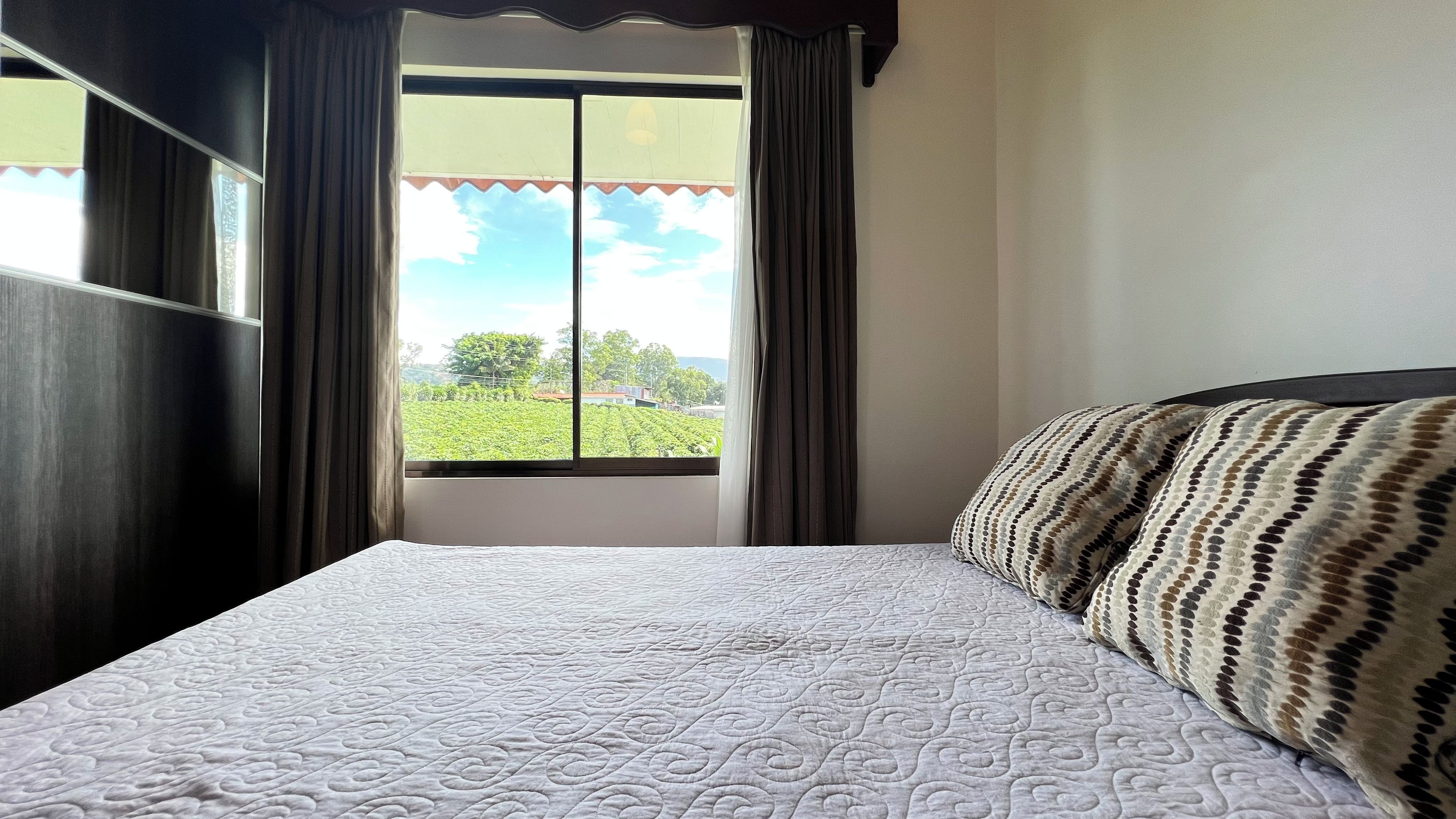 Une chambre avec un lit, une fenêtre avec des rideaux et une vue sur un paysage verdoyant.