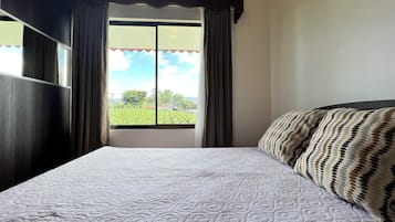 Une chambre avec un lit, une fenêtre avec des rideaux et une vue sur un paysage verdoyant.