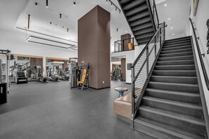 Ein Fitnessstudio mit verschiedenen Trainingsgeräten, einer Treppe und einer Spiegelwand.