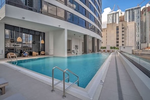 Une piscine sur le toit, dotée d’une balustrade en verre, entourée de bâtiments modernes et surplombant un ciel dégagé.