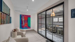 A modern interior with a large abstract painting, a seating area with a sofa and chairs, and a view into a conference room through a glass partition. - Brand New Building & Amazing Amenities (Miami)