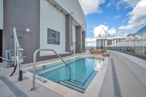 Ein Pool auf dem Dach mit klarem, blauem Wasser, einer Glasbarriere und Blick auf Baukräne im Hintergrund.