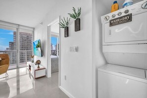 Ein modernes Hotelzimmer mit Balkon, Blick auf die Stadt, einem Wand-Fernseher und einer Waschmaschine.