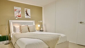 Ein ordentlich bezogenes Bett mit einem Kopfteil, einer Nachttischlampe und zwei Bildern an der Wand.