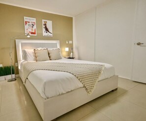 A neatly made bed with a headboard, a bedside lamp, and two posters on the wall. - Basquiat Brickell Luxury Retreat (Miami)