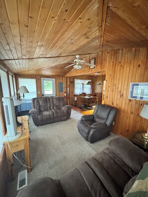 A wooden-paneled room with a ceiling fan, two leather sofas, a television, and a dining area in the background. - 2 Bedroom cabin in the heart of the Hiawatha National Forest... (Manistique)