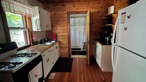 Una cucina compatta con pareti in legno, un fornello, un frigorifero e una finestra con tende.