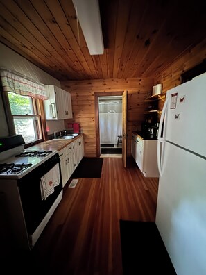 A compact kitchen with wooden walls, a stove, a refrigerator, and a window with curtains. - 2 Bedroom cabin in the heart of the Hiawatha National Forest... (Manistique)
