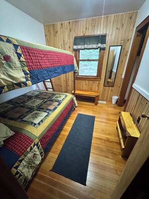 A room with a bunk bed, a small bench, a window with a view, and a mirror.