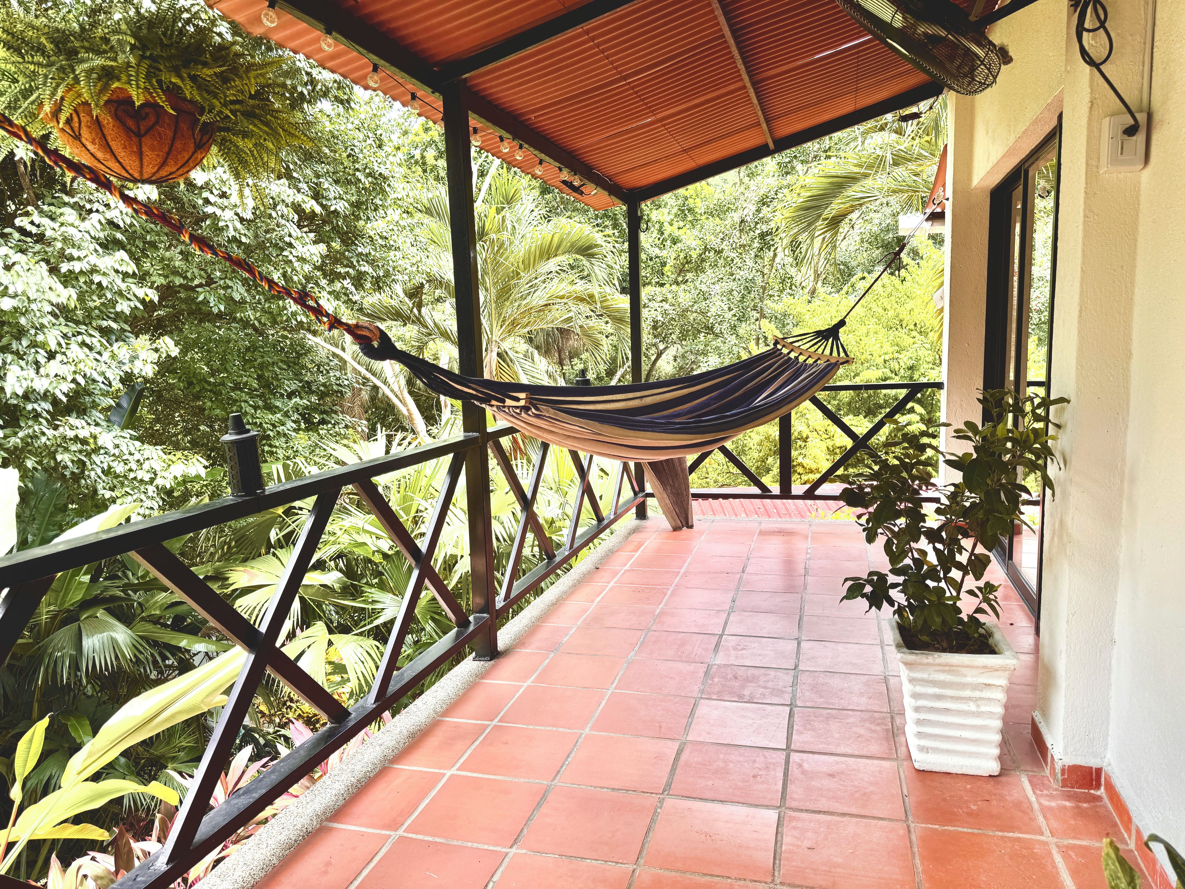 A hammock under a tiled roof, surrounded by greenery.