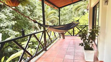 A hammock under a tiled roof, surrounded by greenery.