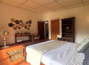 Ein Schlafzimmer mit einem Bett, einem Nachttisch, einem Ventilator, einem Kleiderschrank und einer mit Tellern dekorierten Wand.