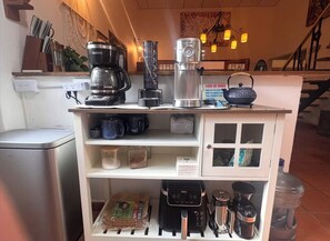 Une petite cuisine équipée d’une machine à café, d’un mixeur et d’un distributeur d’eau. On y trouve également des étagères avec des tasses et un petit réfrigérateur.