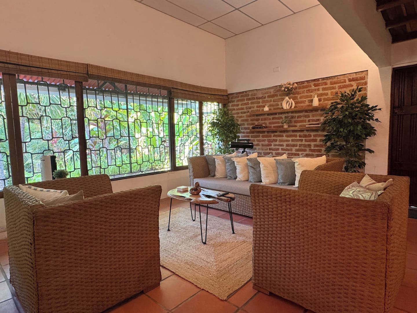 A living room with a sofa, two armchairs, a coffee table, and a large window with a view of greenery.