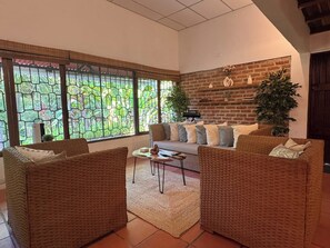 A living room with a sofa, two armchairs, a coffee table, and a large window with a view of greenery.