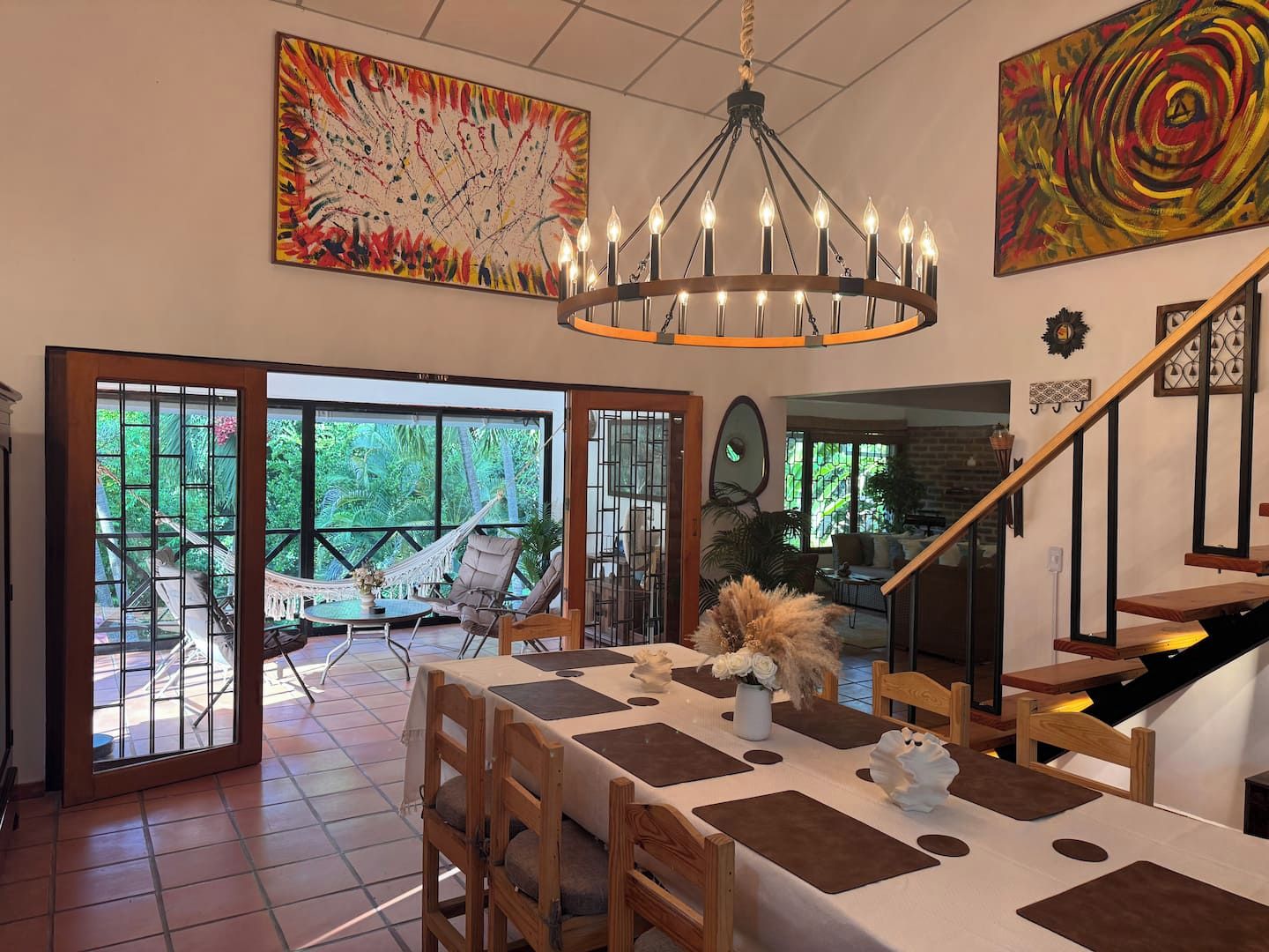 A dining area with a table set for four, a chandelier, and a view of the outdoors through large glass doors.