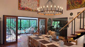 A dining area with a table set for four, a chandelier, and a view of the outdoors through large glass doors.