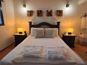 Une chambre d’hôtel avec un grand lit, deux tables de chevet avec des lampes, une tête de lit et des œuvres d’art accrochées au mur.