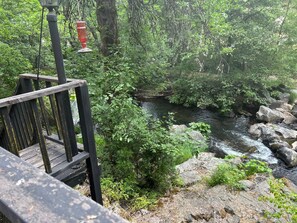 A wooden deck overlooking a natural stream with rocks and greenery. - Historic Kanary Lodge : Private Riverfront Retreat (Wilseyville)