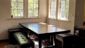 Ein Zimmer mit einem großen Tisch, zwei Bänken und drei Fenstern mit Blick auf Bäume.