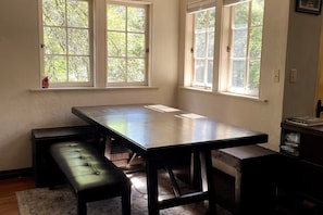 Ein Zimmer mit einem großen Tisch, zwei Bänken und drei Fenstern mit Blick auf Bäume.