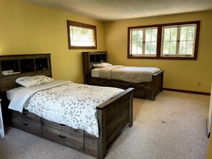 A bedroom with two beds, a wooden headboard, a nightstand, and a window with blinds. - Historic Kanary Lodge : Private Riverfront Retreat (Wilseyville)