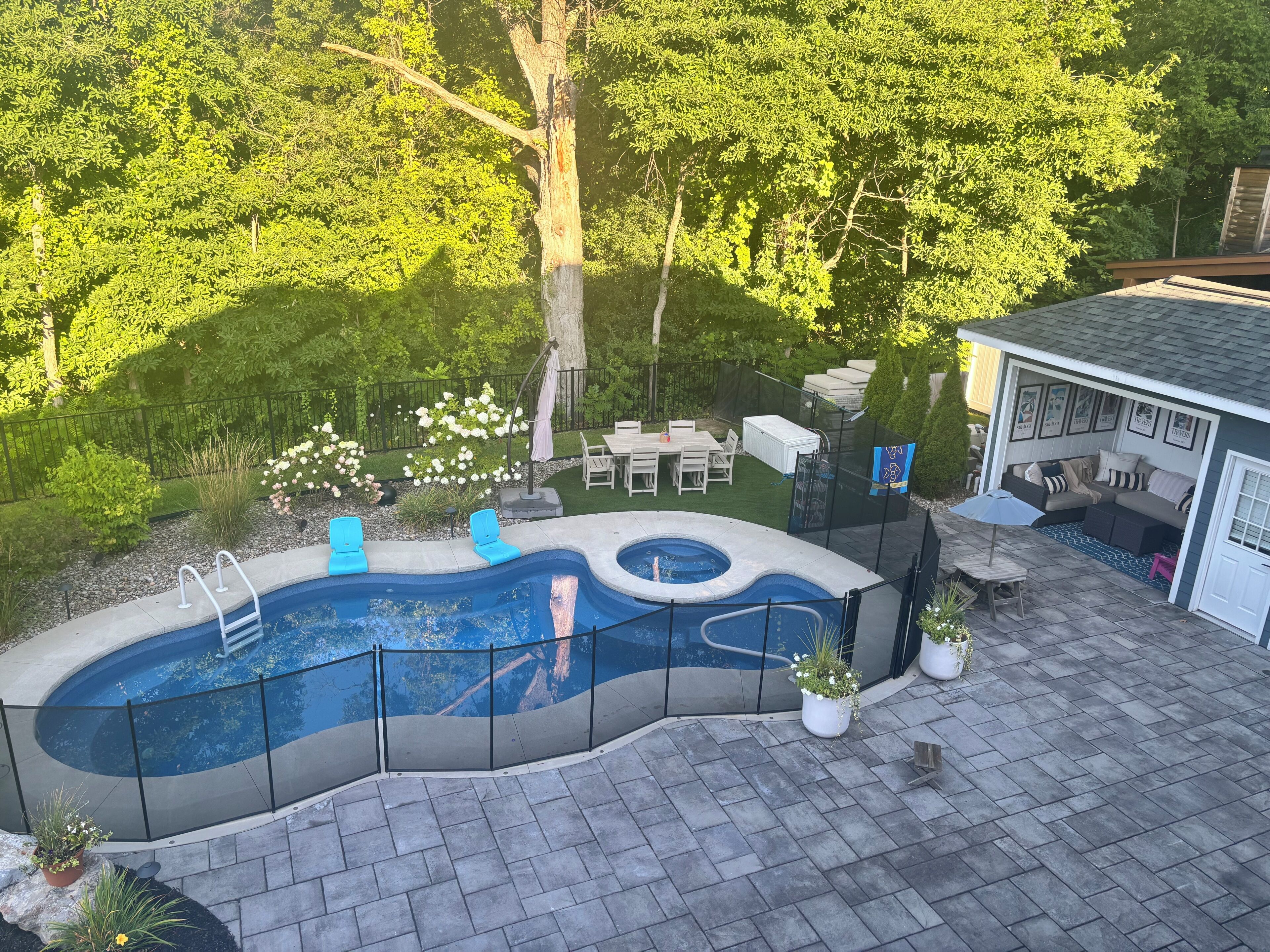 Ein Garten mit Schwimmbad, Terrassenmöbeln und einer überdachten Sitzgelegenheit.