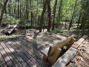 A wooden deck with a bench, surrounded by a forested area with a stream. - Creekside cabin in heart of the Cherokee National Forest on 4 private acres (Reliance)
