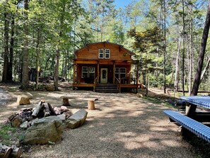 A wooden cabin with a porch, surrounded by trees and a gravel area with picnic tables. - Creekside cabin in heart of the Cherokee National Forest on 4 private acres (Reliance)