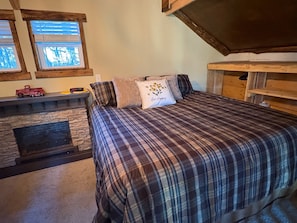 A bedroom with a plaid bedspread, a fireplace, and a window with blinds. - Creekside cabin in heart of the Cherokee National Forest on 4 private acres (Reliance)