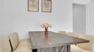 Uma sala de jantar com uma mesa de madeira, seis cadeiras estofadas e duas obras de arte emolduradas na parede.