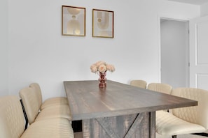 Uma sala de jantar com uma mesa de madeira, seis cadeiras estofadas e duas obras de arte emolduradas na parede.