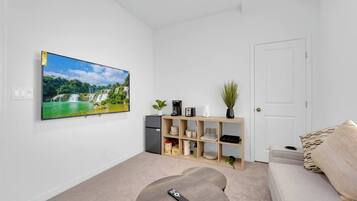 Uma sala de estar com televisão de tela plana na parede, uma mesinha de centro, um sofá e um armário com diversos objetos.
