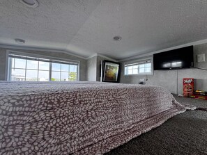 Quarto com uma cama grande, televisão de tela plana na parede e janela com vista para o exterior.