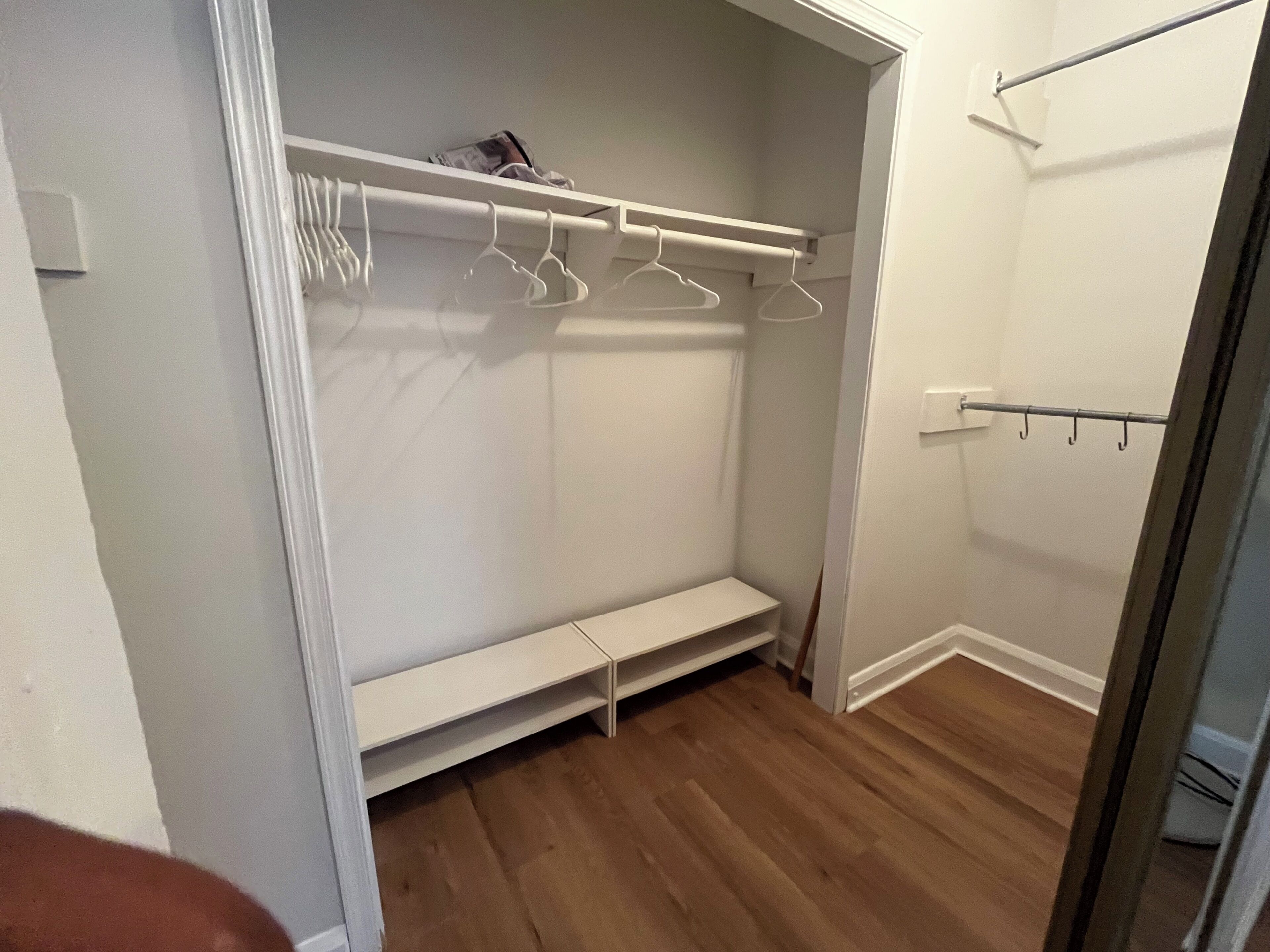 Un dressing accessible sans porte, doté d’un plancher en bois, de murs blancs et d’une tringle pour suspendre les vêtements.