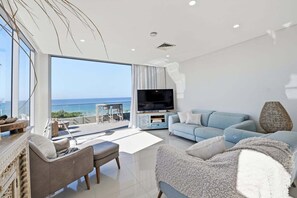 Ein modernes Wohnzimmer mit großem Fernseher, einer Couch und einem Balkon mit Meerblick.